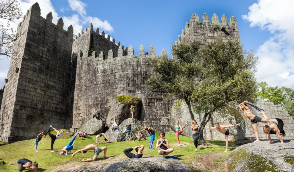 A group of practitioners demonstrating various postures from the e84 Intermediate and 84 Asanas series in front of a castle.