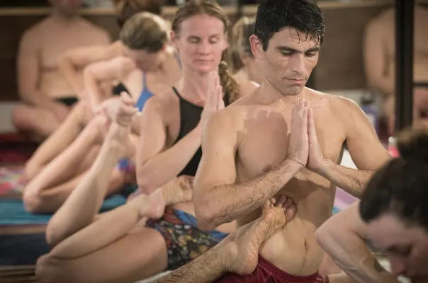A man in deep focus holding a seated posture with hands in prayer during a yoga teaching training class.