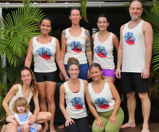 A group of yoga trainees and a child posing in matching “26&2” logo shirts during a best yoga teacher training program.