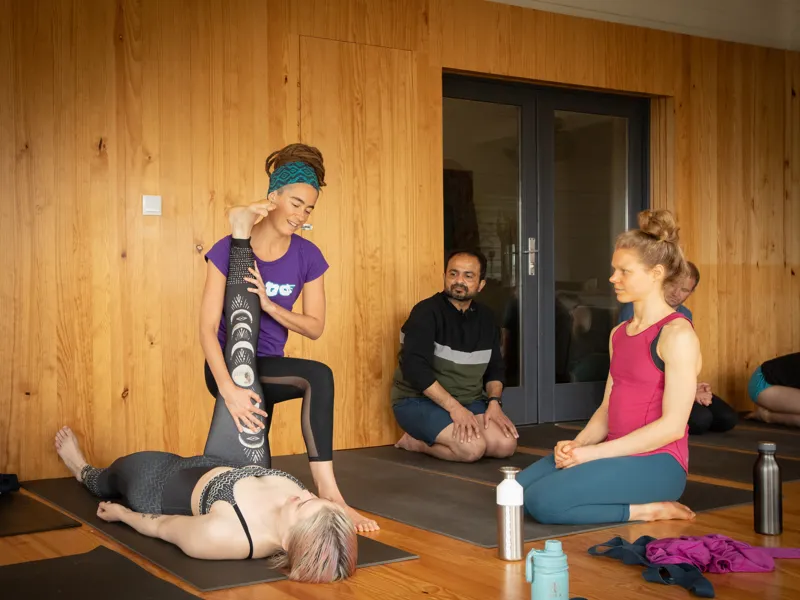 A yoga instructor providing hands-on guidance to a student during a leg stretch to ensure a safe and proper alignment.